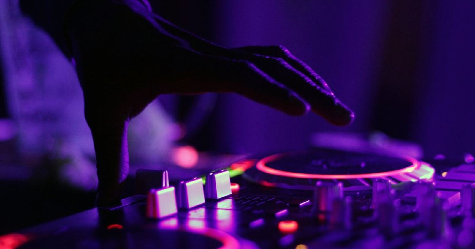A DJ mixing at a set of decks lit in deep purple