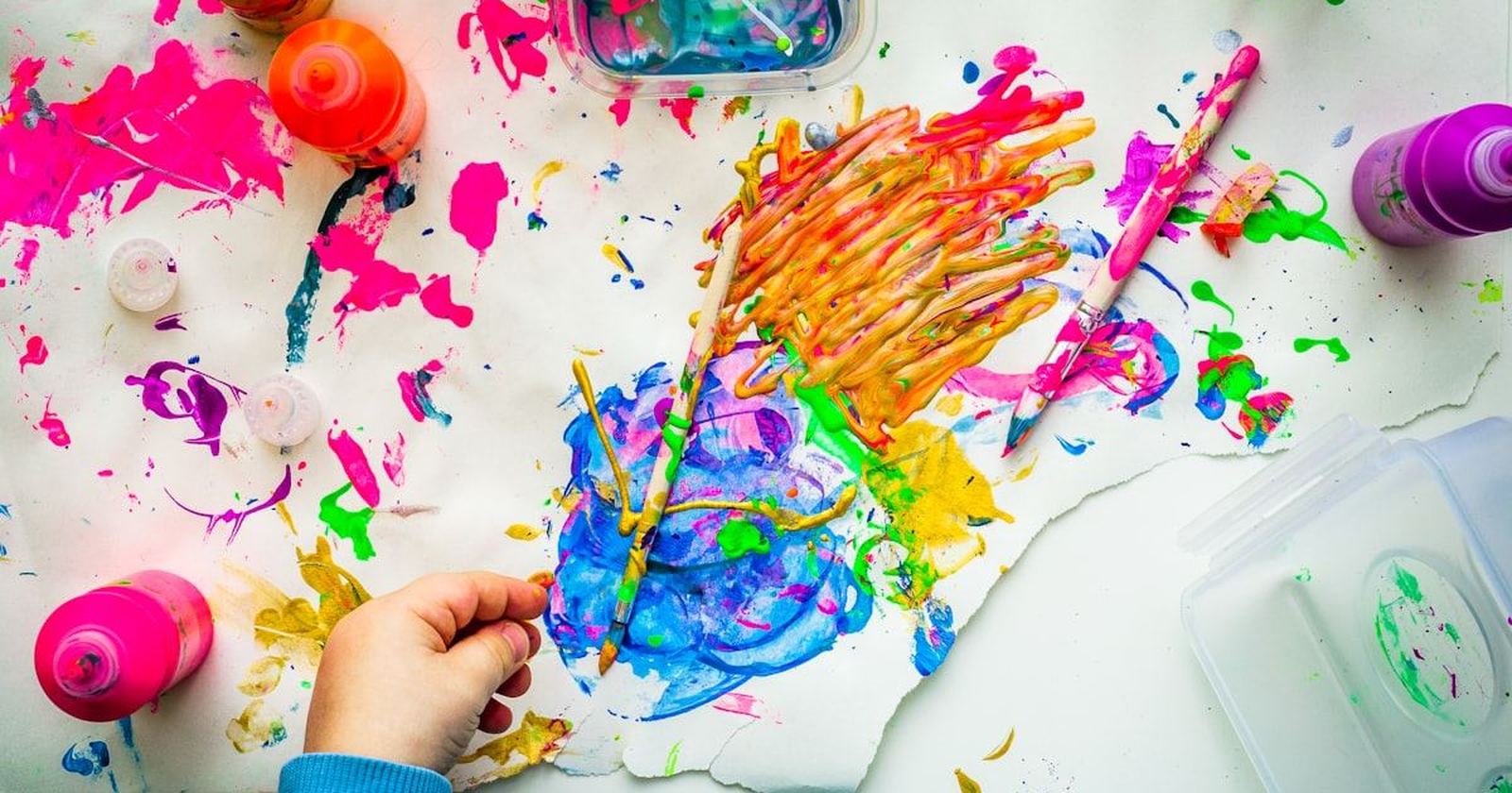 A child painting in bright colors, brushes and paint scattered across the table