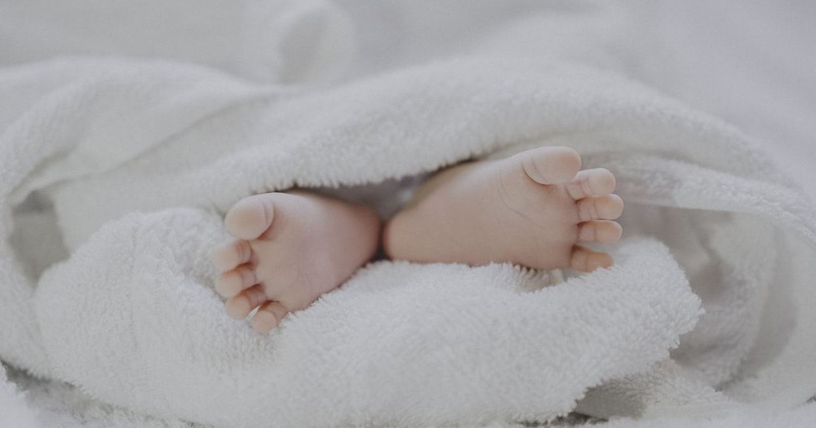 A newborn baby’s feet resting in a soft white blanket