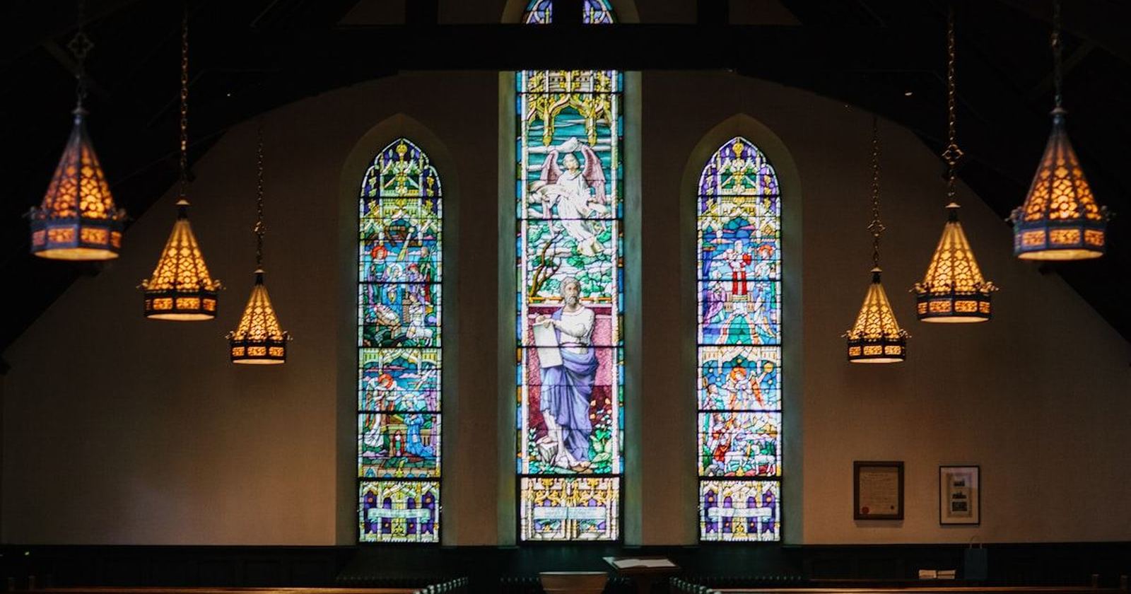 The interior of a church, sunlight falling through tall stained glass windows