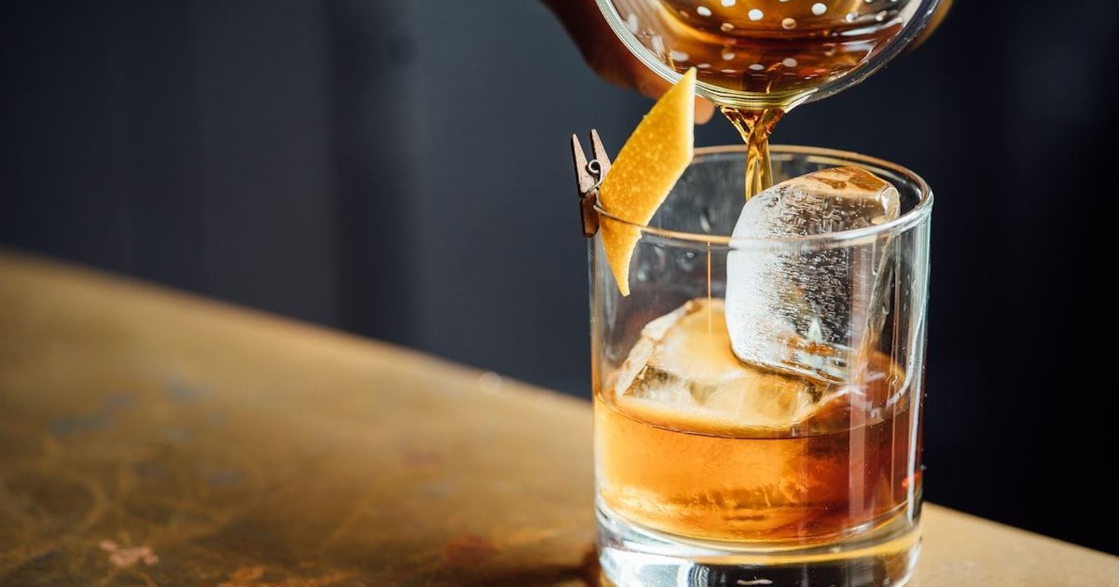 A cocktail being poured over ice in a heavy tumbler