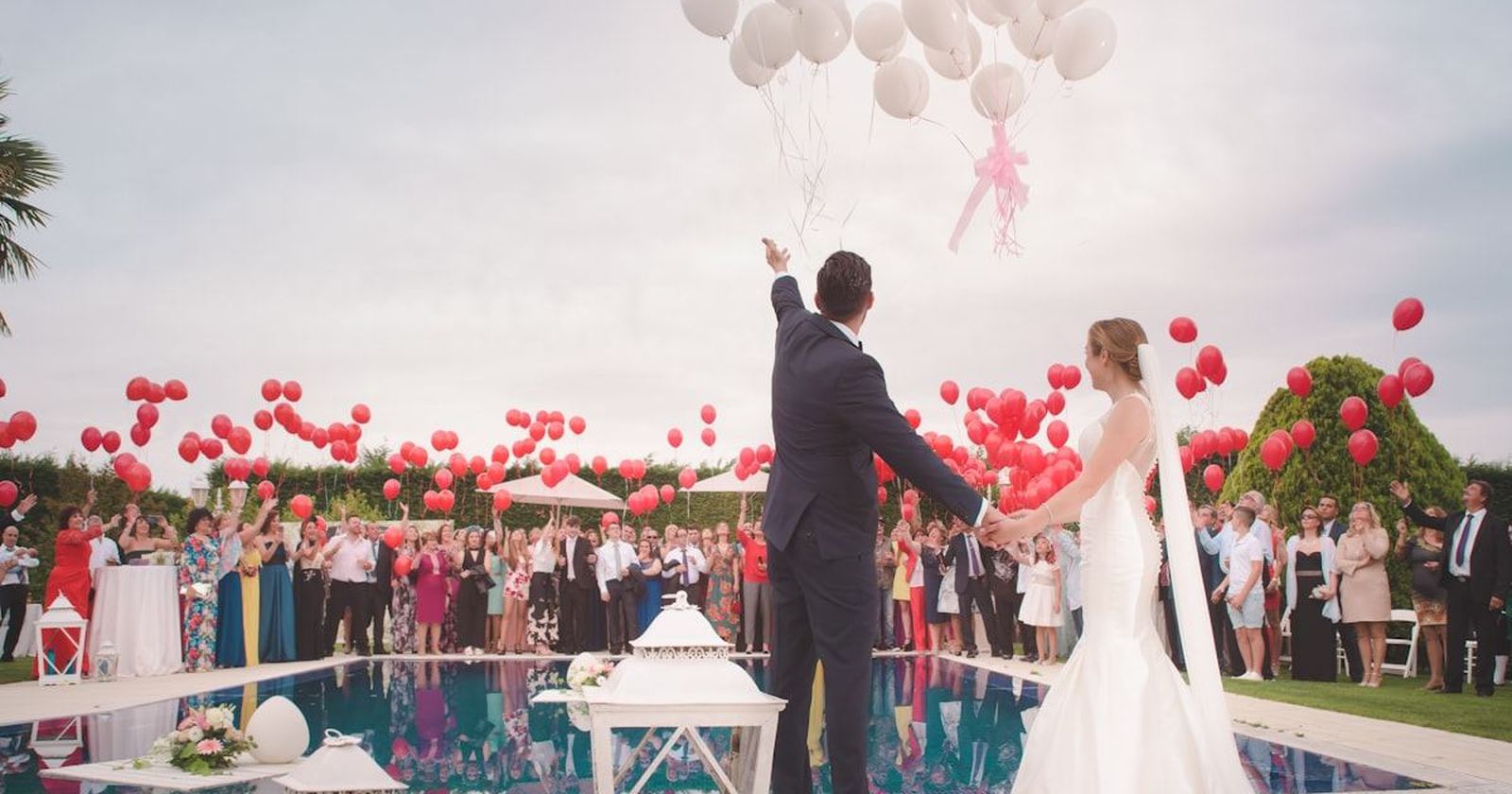 A wedding ceremony outdoors as guests release balloons above the couple