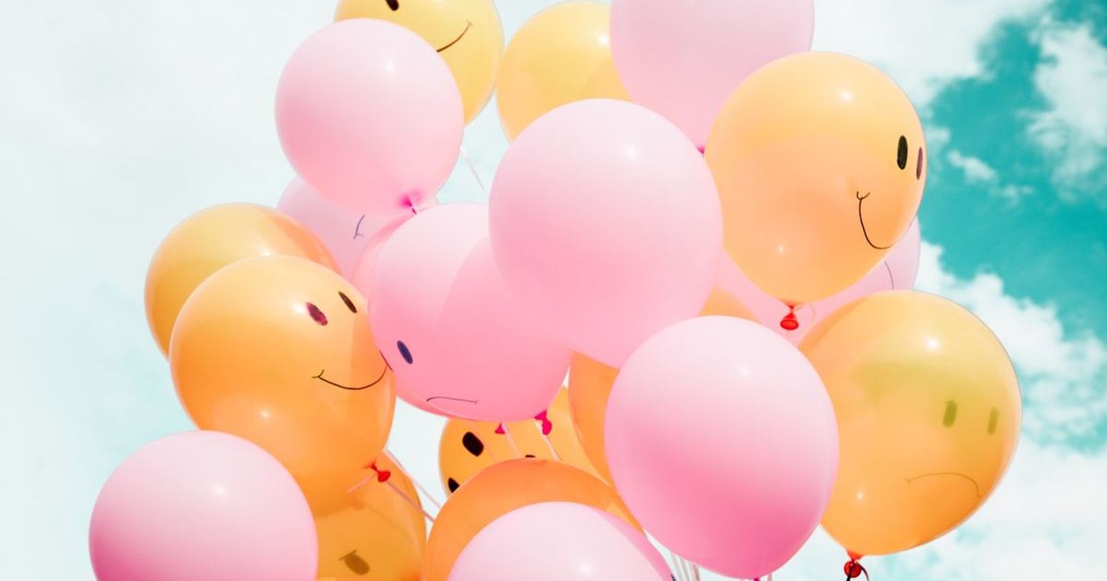 A cluster of pink and orange balloons against a pale sky