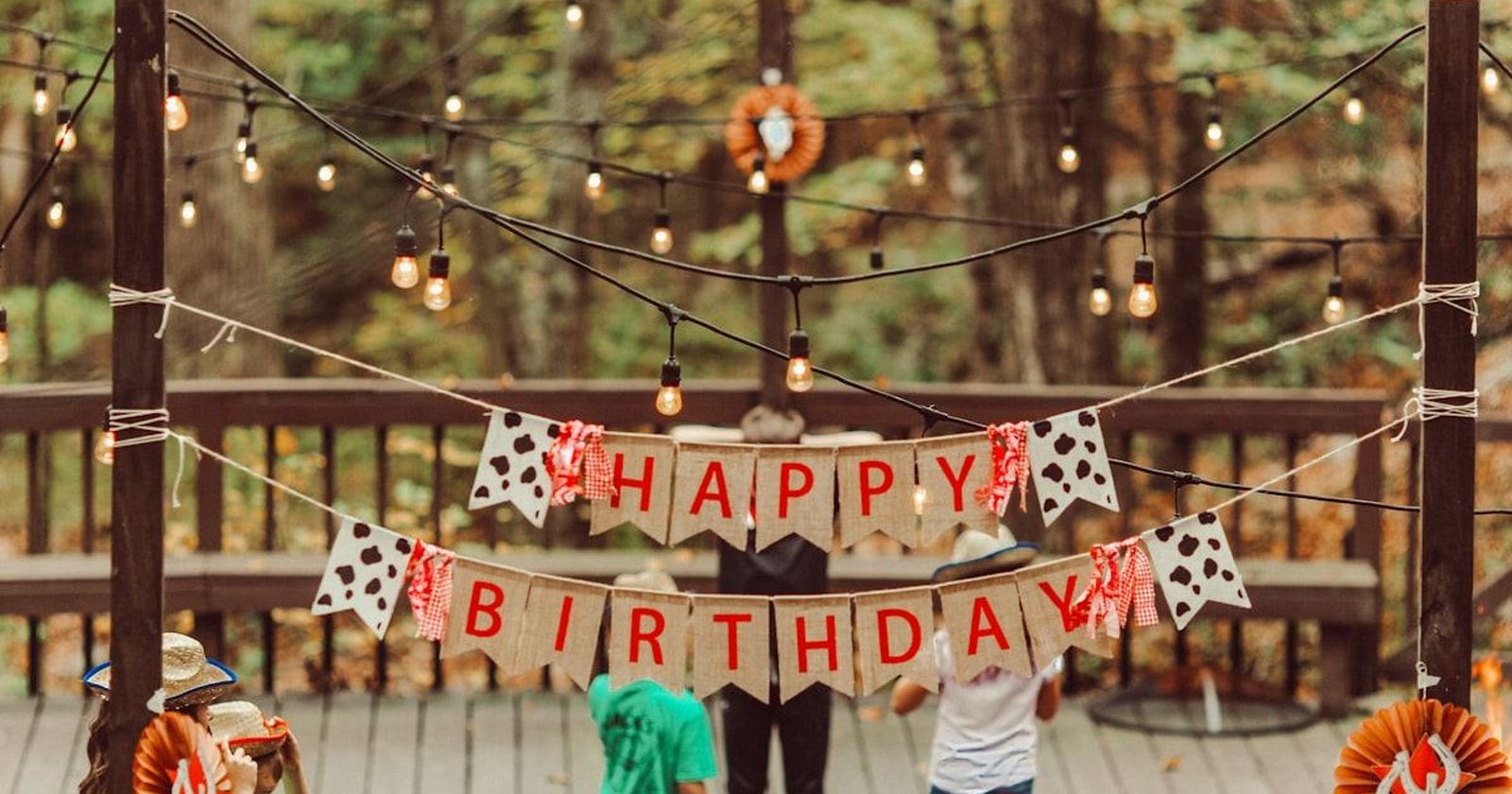 A hand-lettered happy birthday banner strung between trees at an outdoor party