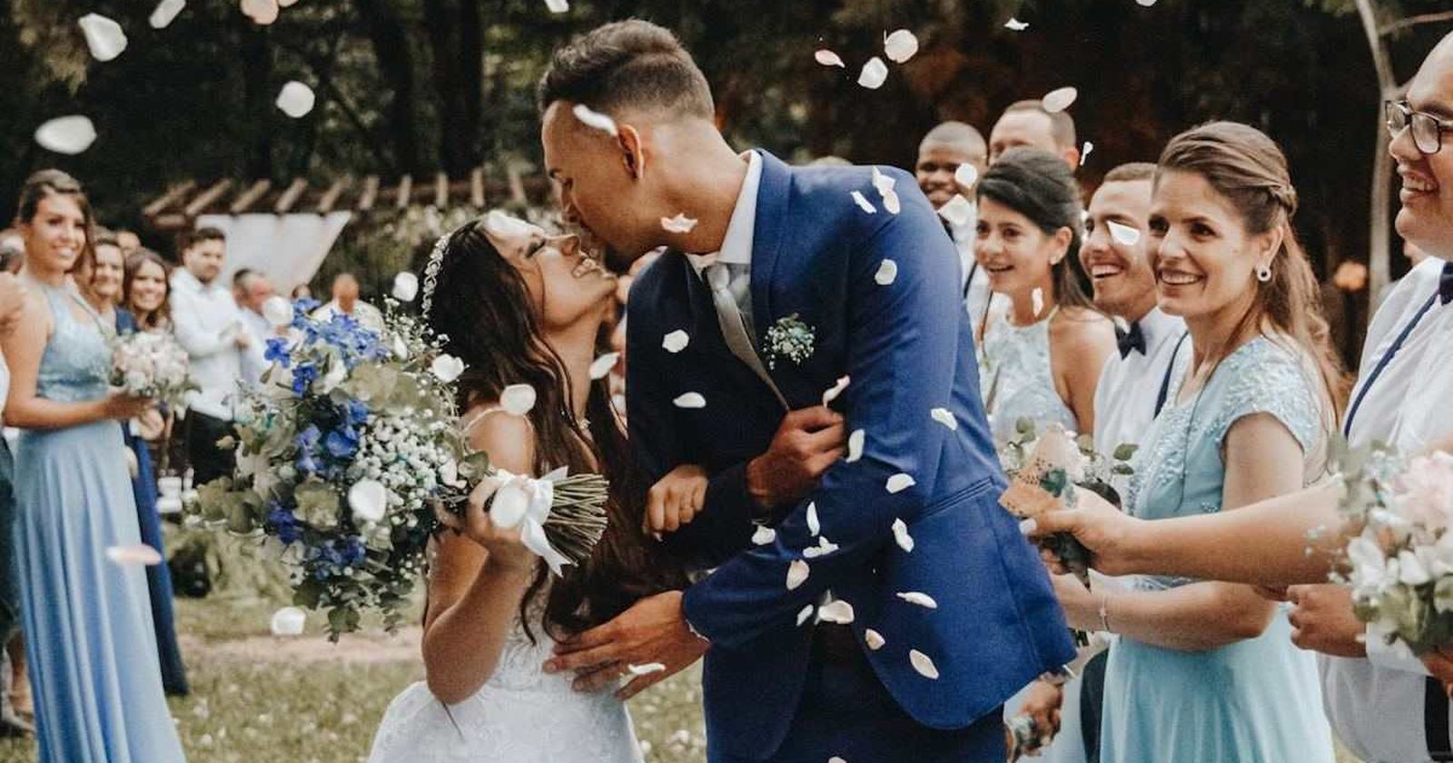 A couple kissing in a shower of confetti while their guests cheer around them