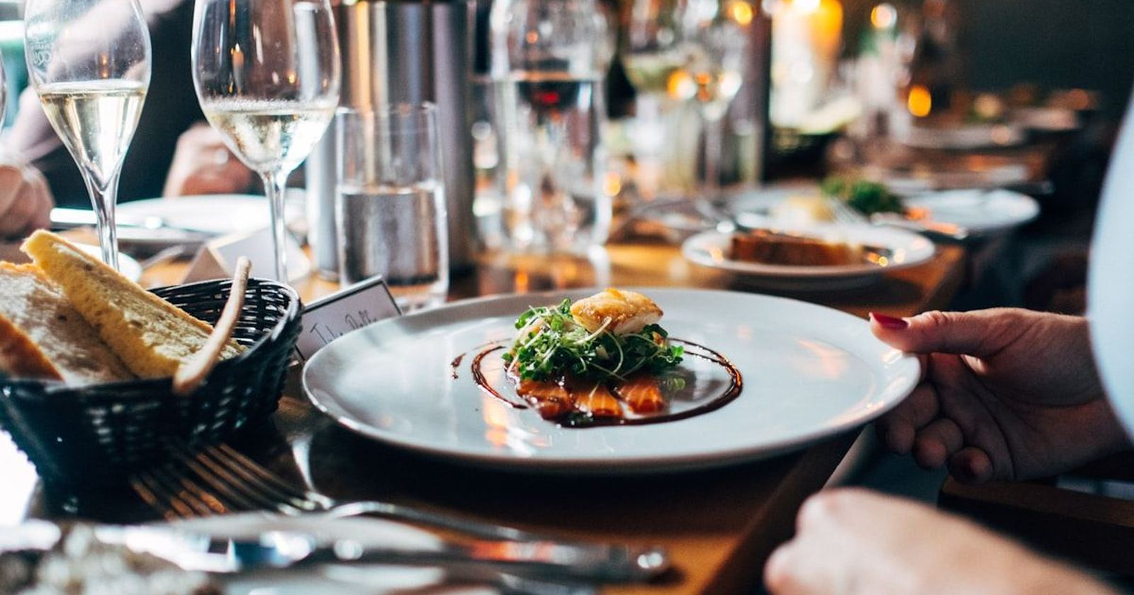 A formal dinner place setting with wine glasses and a plated first course
