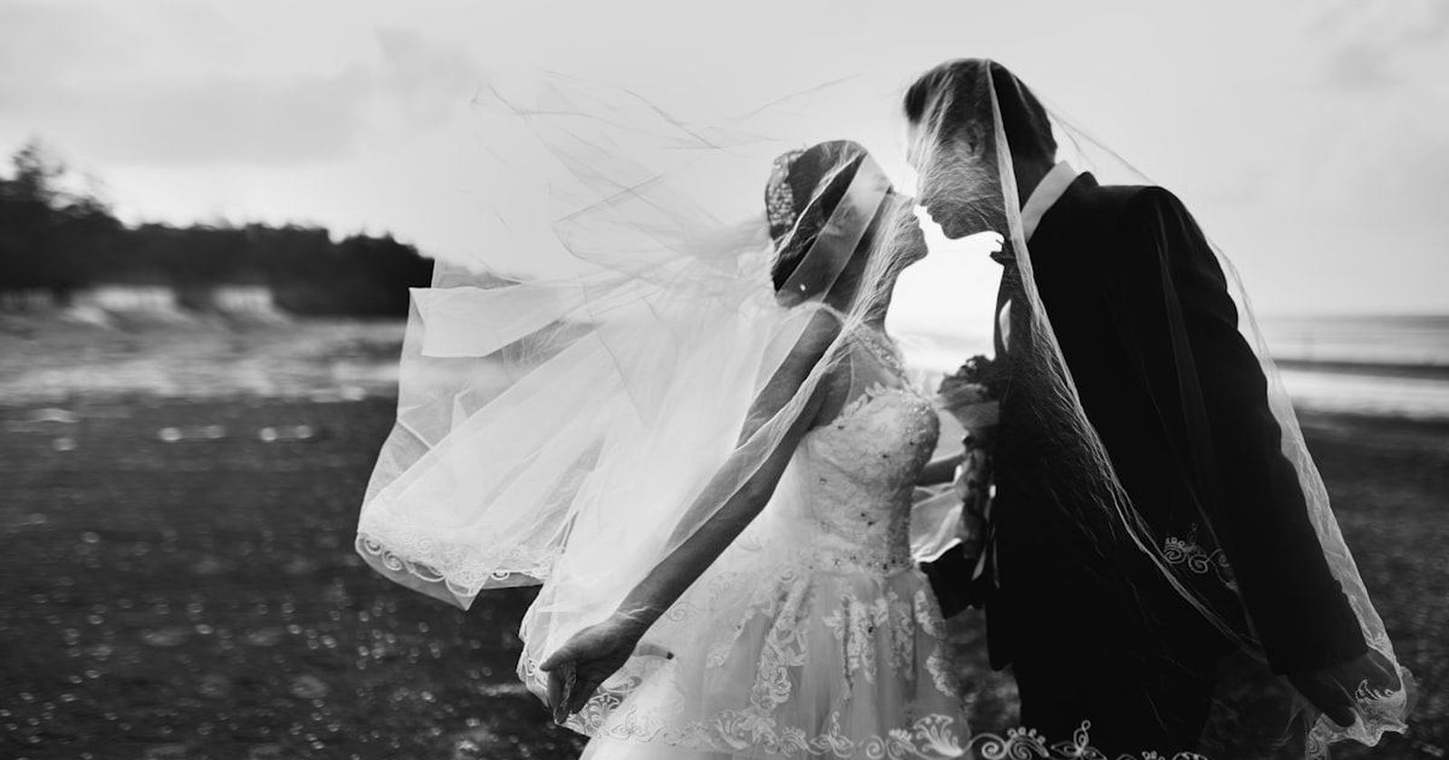A black and white photograph of a couple sheltered beneath a flowing veil