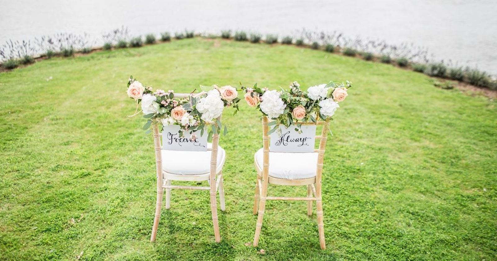 Two ceremony chairs decorated with flowers, set on a lawn before the guests arrive